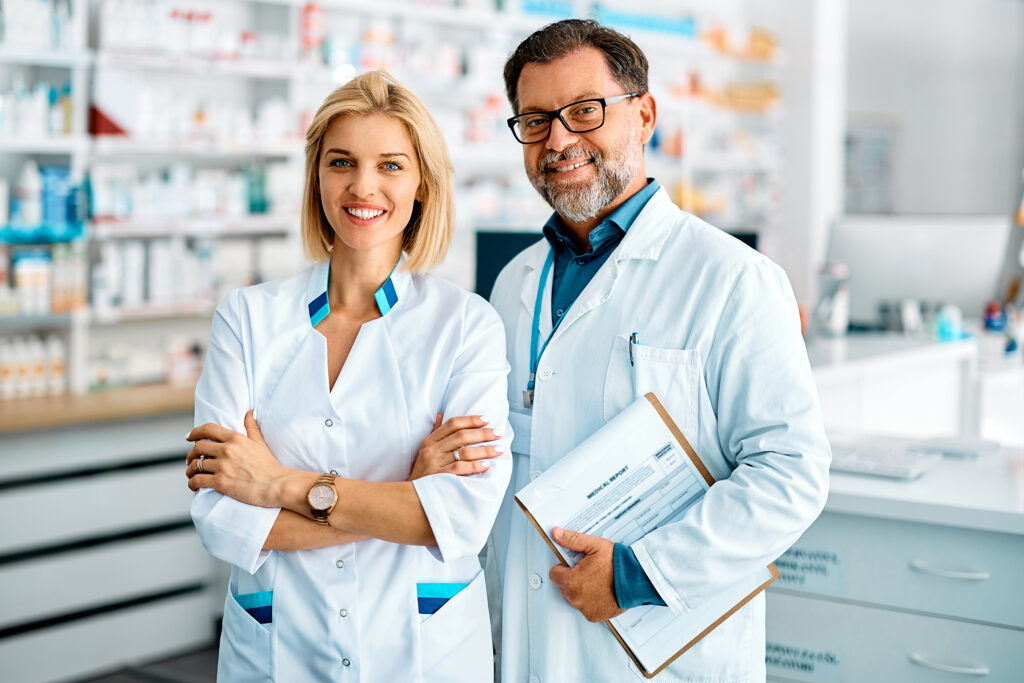 Portrait of confident pharmacist and her mature coworker in pharmacy and looking at camera.